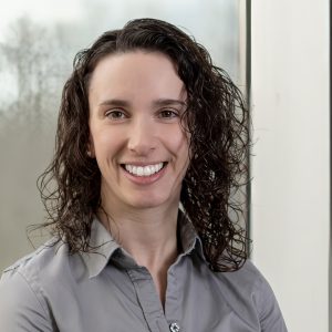 Smiling woman with curly dark hair wearing a gray collared shirt