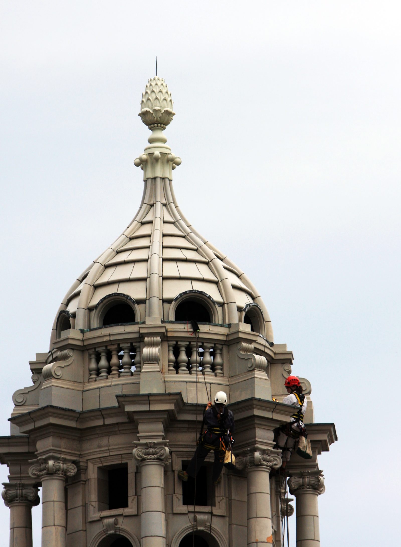Rope-access workers inspect the ornate dome and spire of a historic building
