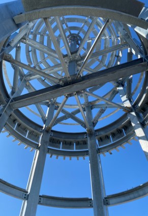 Steel framework of a large circular structure viewed from below against a blue sky
