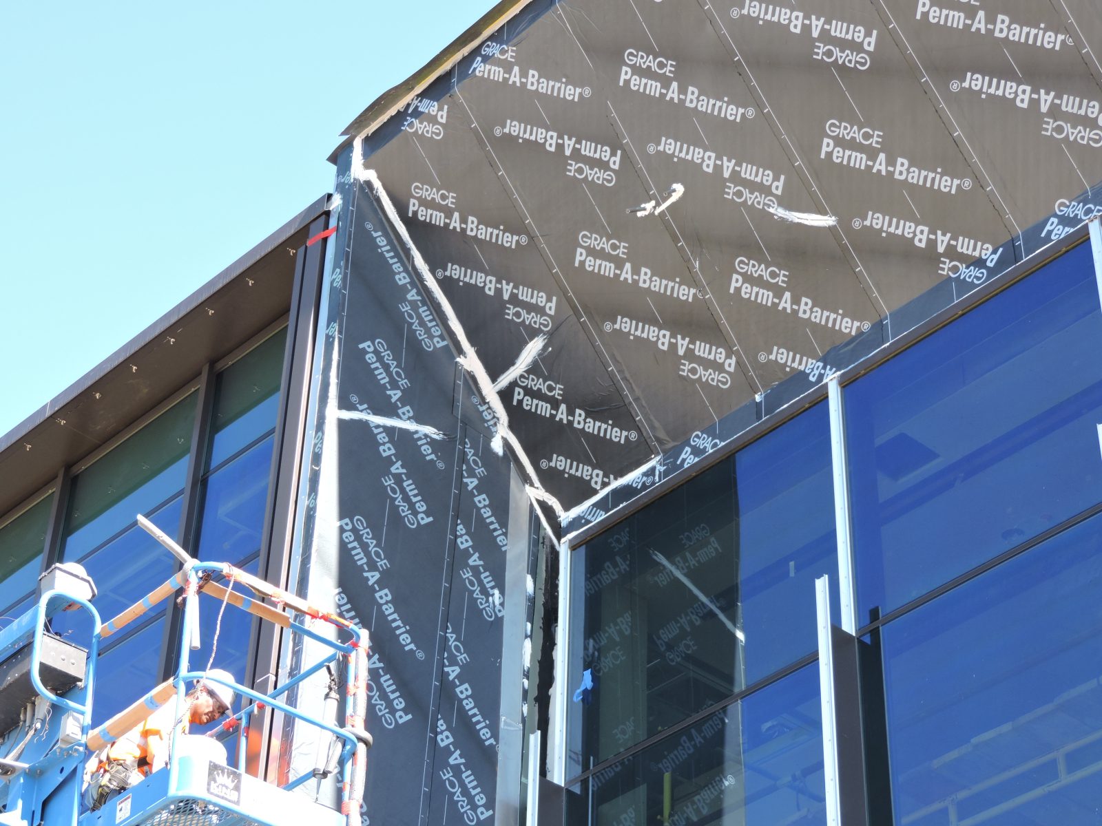 Building under construction with GRACE Perm-A-Barrier membrane, glass windows, and a worker on a lift
