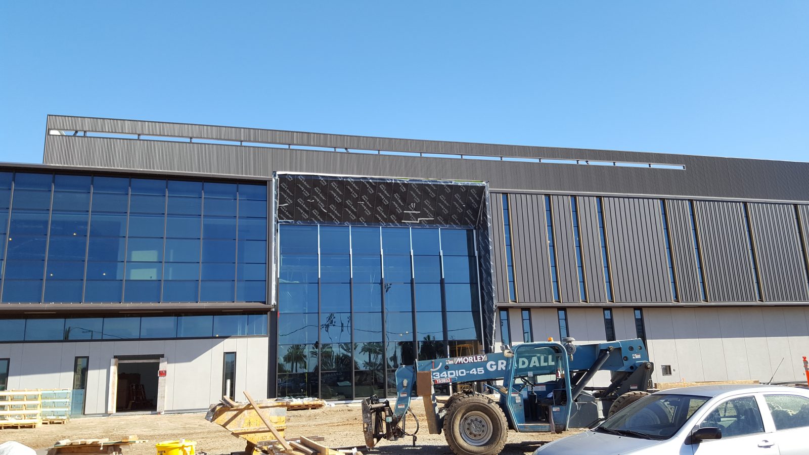 Modern commercial building under construction, with a blue telehandler parked in front