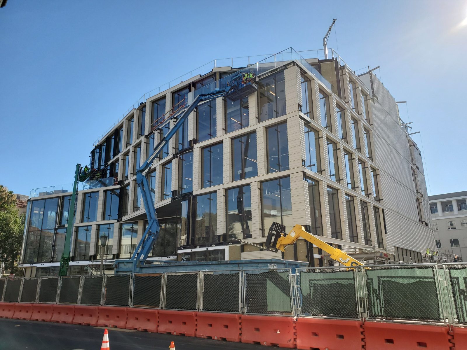 Modern multi-story building under construction, with workers, lifts, and construction barriers along the street