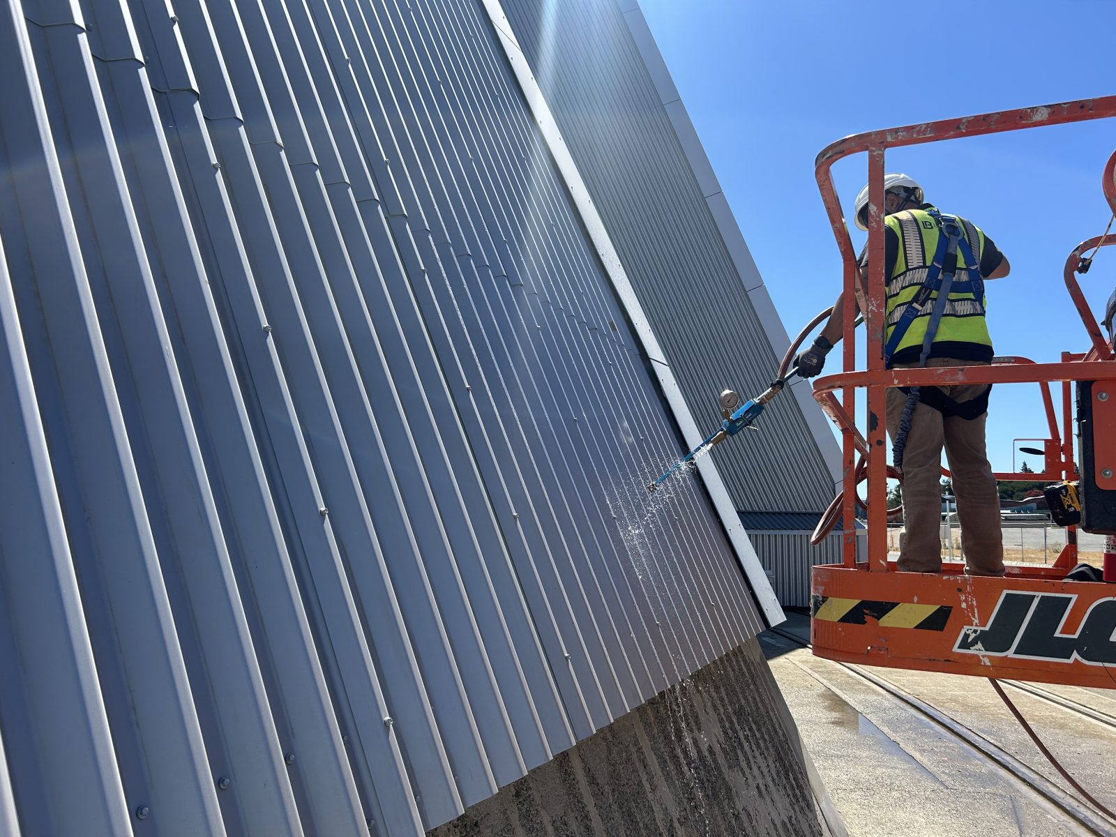 Worker in a lift pressure-washes the corrugated metal exterior of a building