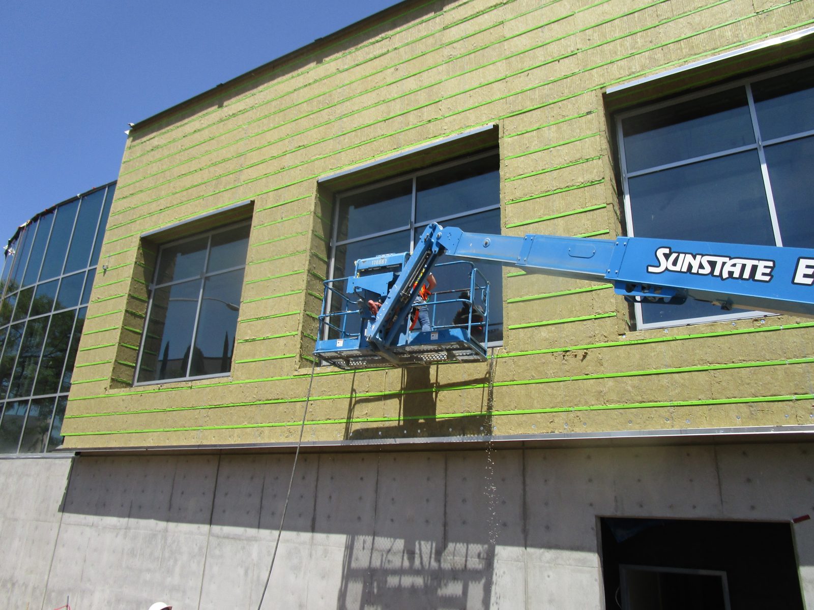Worker in a blue lift platform installs insulation on a building facade