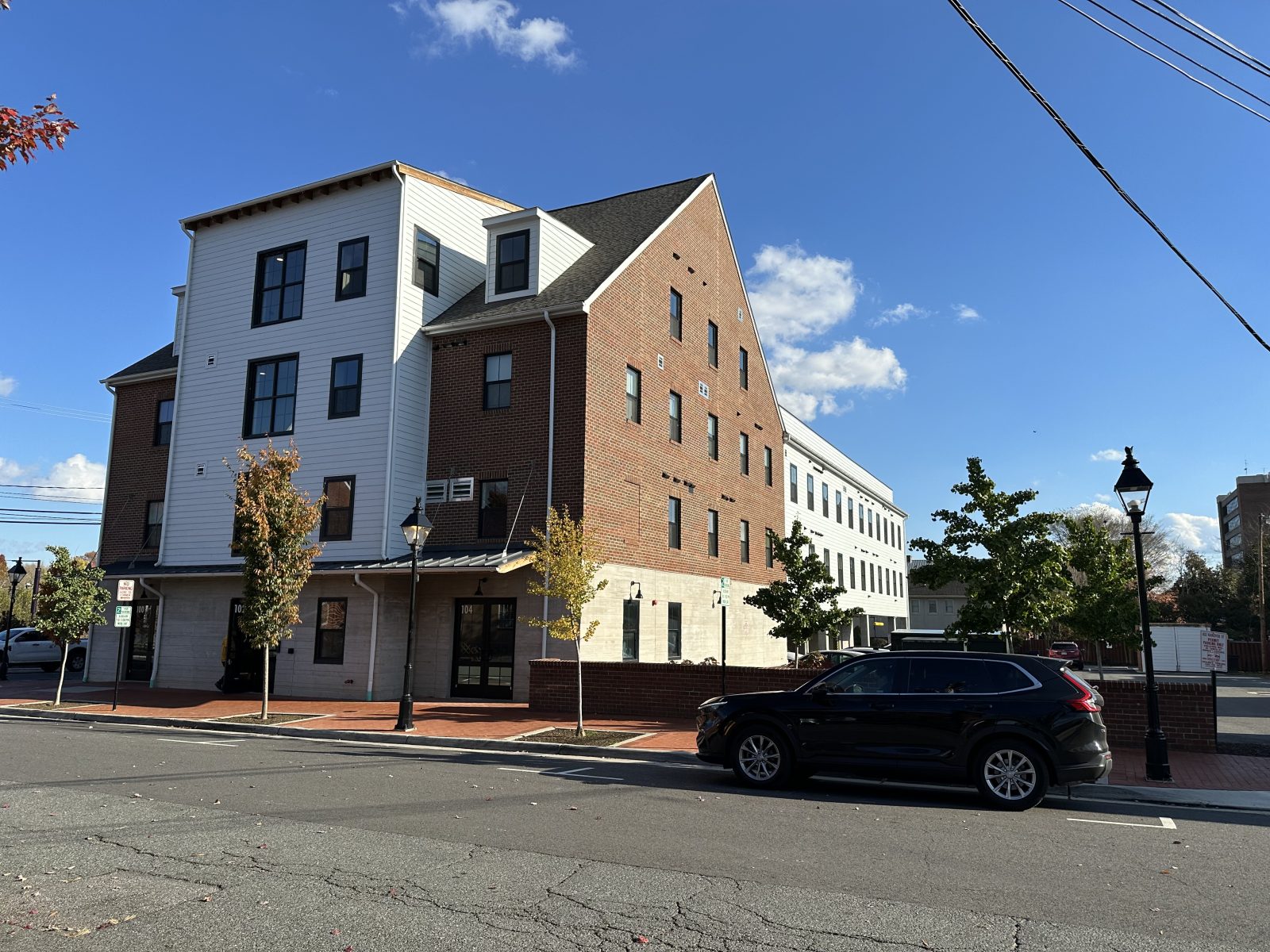 Mixed brick-and-white multi-story building along a tree-lined urban street under a blue sky