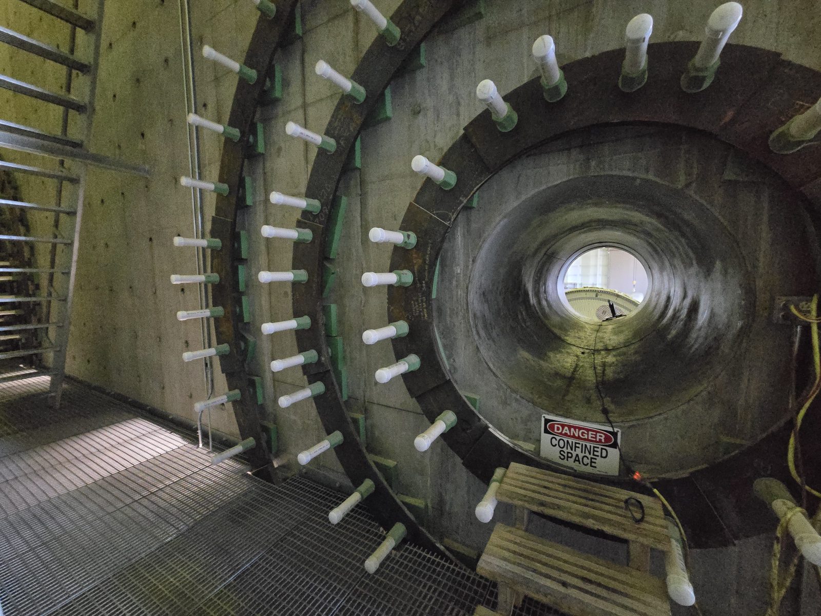 Industrial tunnel with rows of white bolts and a “Danger Confined Space” warning sign