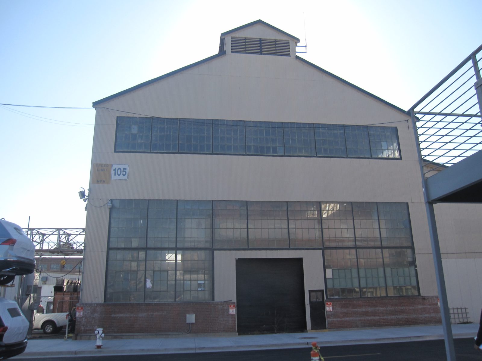 Large industrial warehouse with rows of windows, a garage door, and a visible speed limit 105 MPH sign