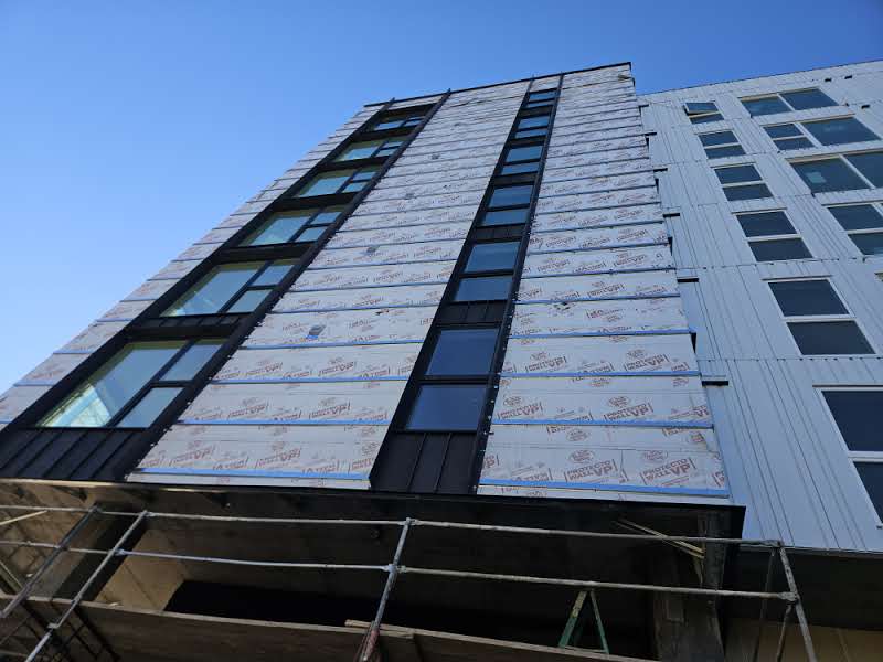 Multi-story building under construction with exposed insulation, windows, and scaffolding