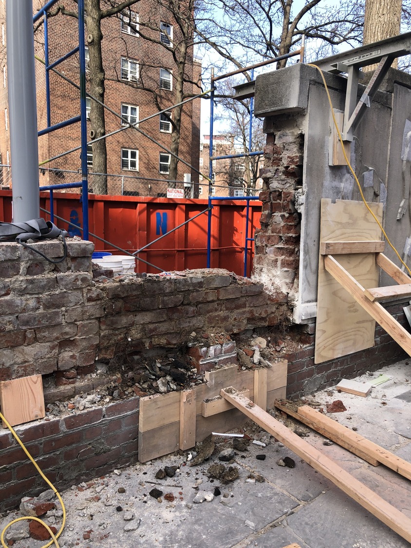 Construction site with a partially demolished brick wall, exposed masonry, scaffolding, and debris
