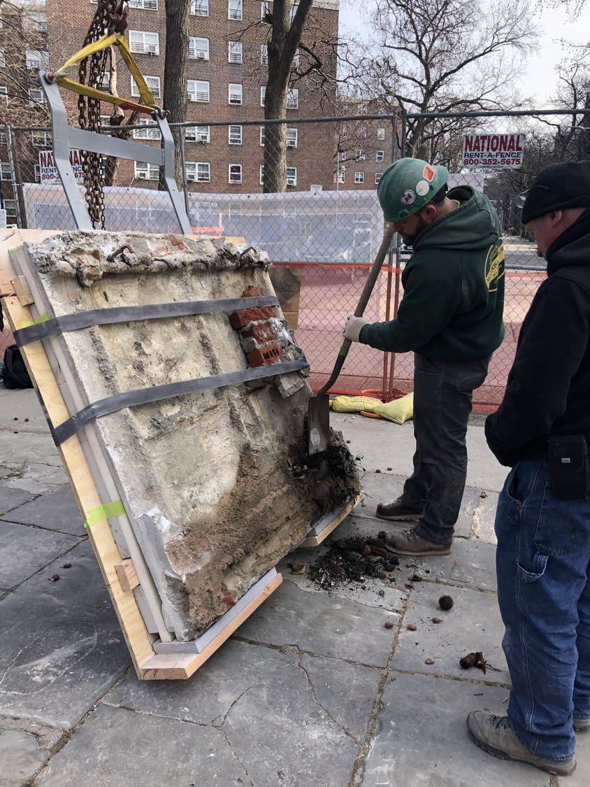 Construction workers dismantle a large section of brick-and-concrete wall at a construction site