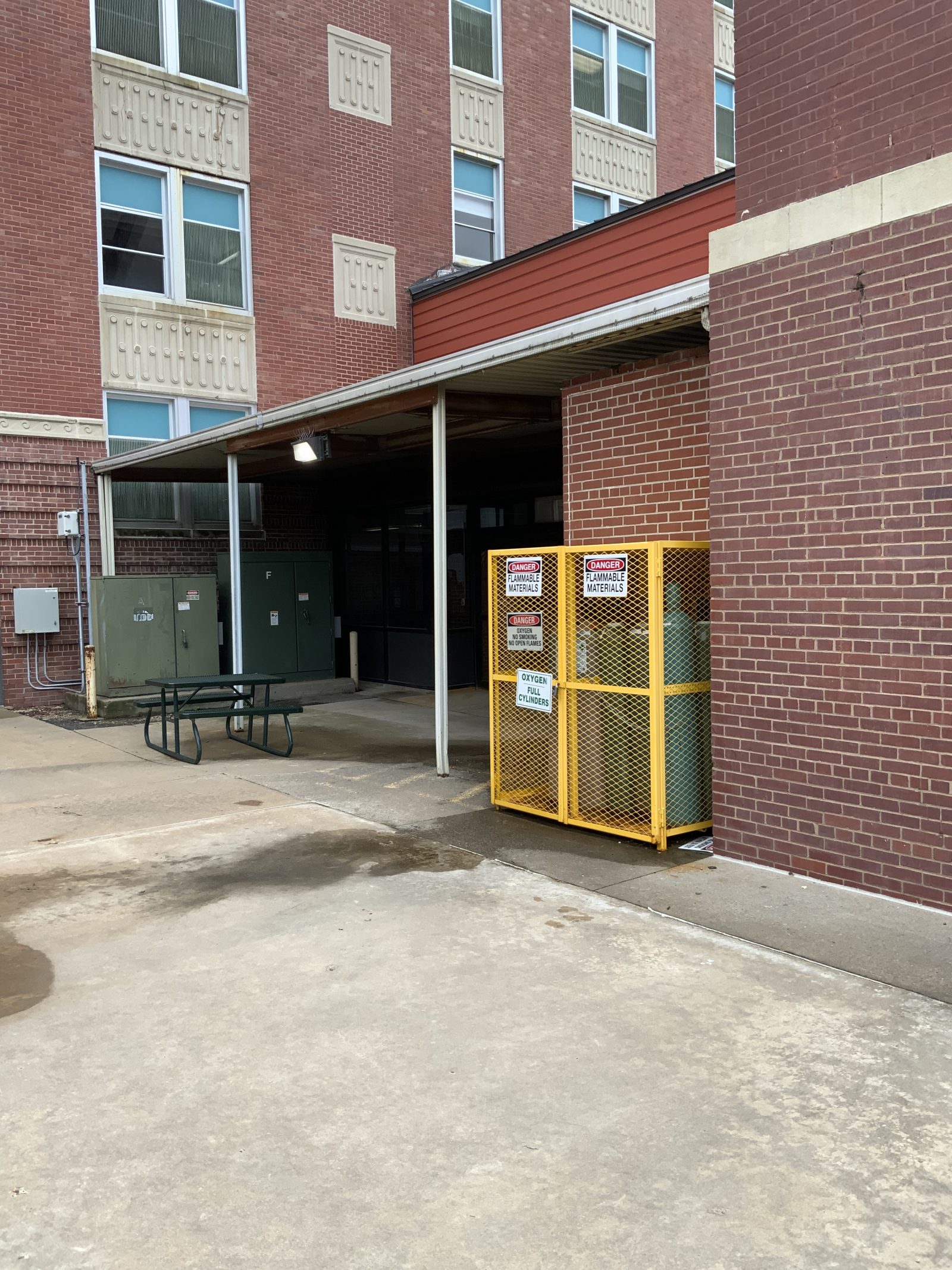 Brick building service area with a yellow enclosure labeled “Danger: flammable materials” and “Oxygen: full cylinders.”