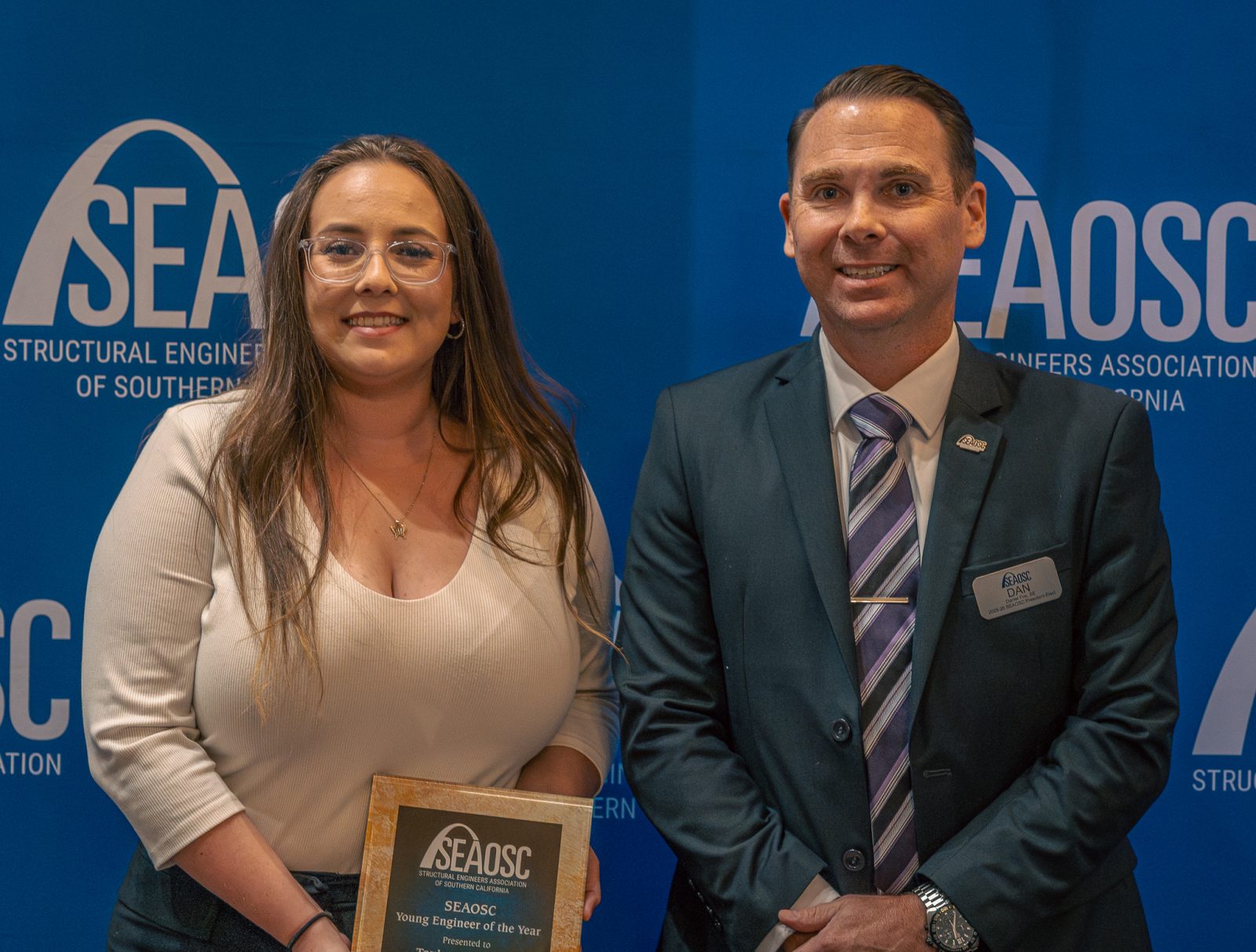 A woman holds a SEAOSC Young Engineer of the Year award beside a man in a suit at a SEAOSC event