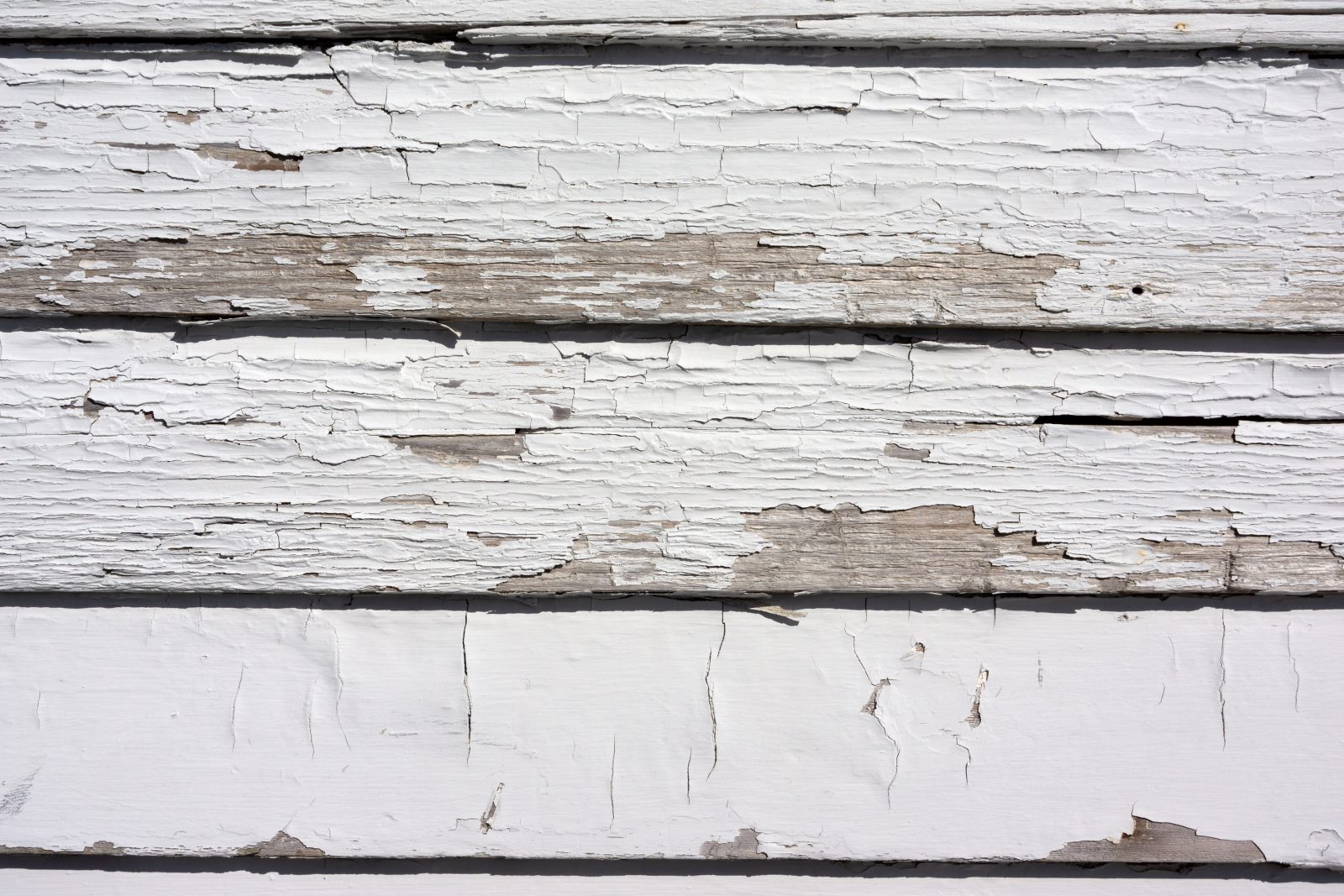 Badly worn paint on wood siding showing peeling and cracking