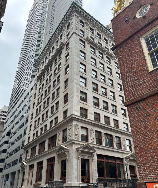 Ornate historic stone building with detailed facades and tall windows, flanked by modern skyscrapers and a brick church