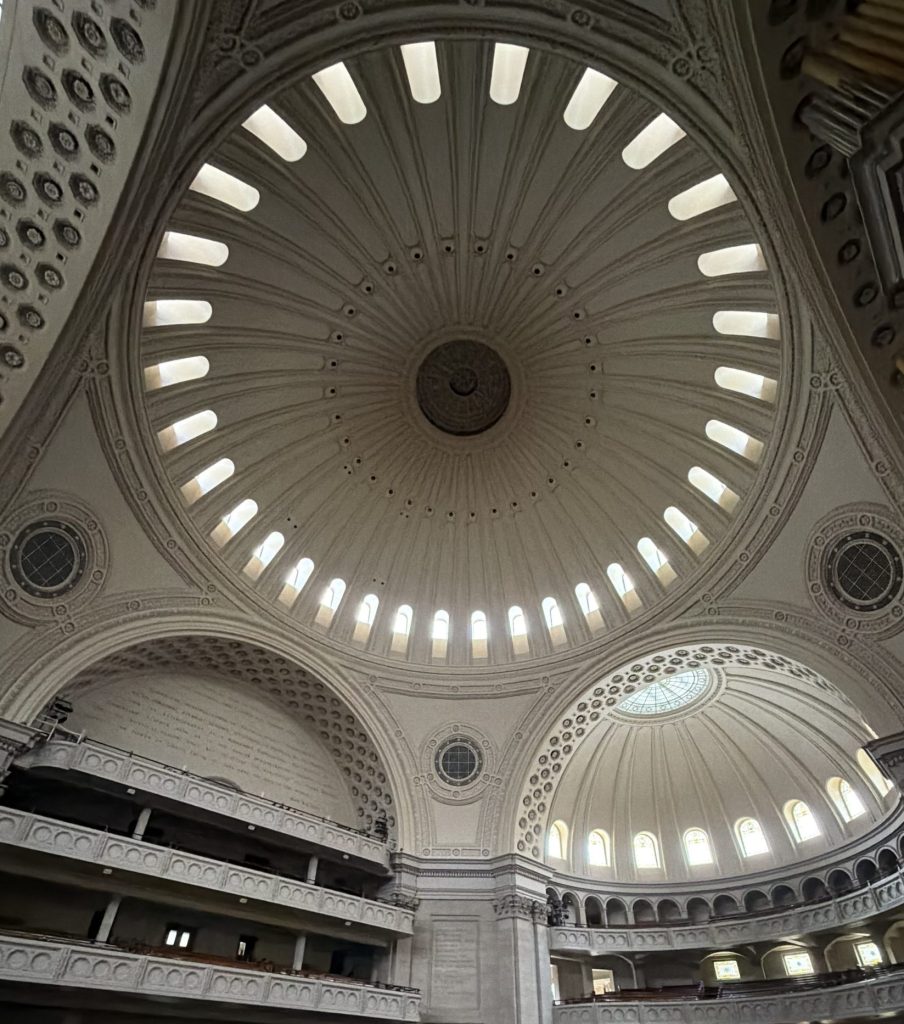 Ornate domed interior with a central oculus, radiating skylights, arched windows, balconies, and decorative plasterwork