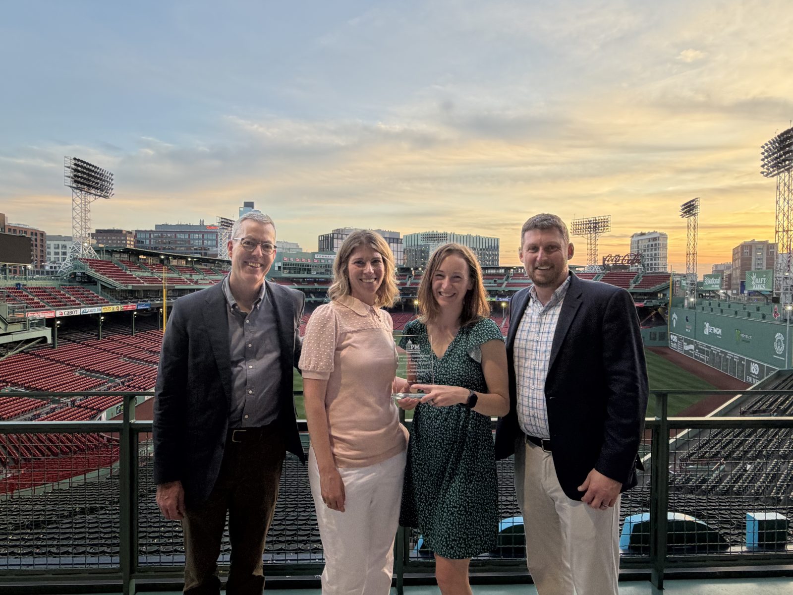 Four people pose together at Fenway Park during sunset