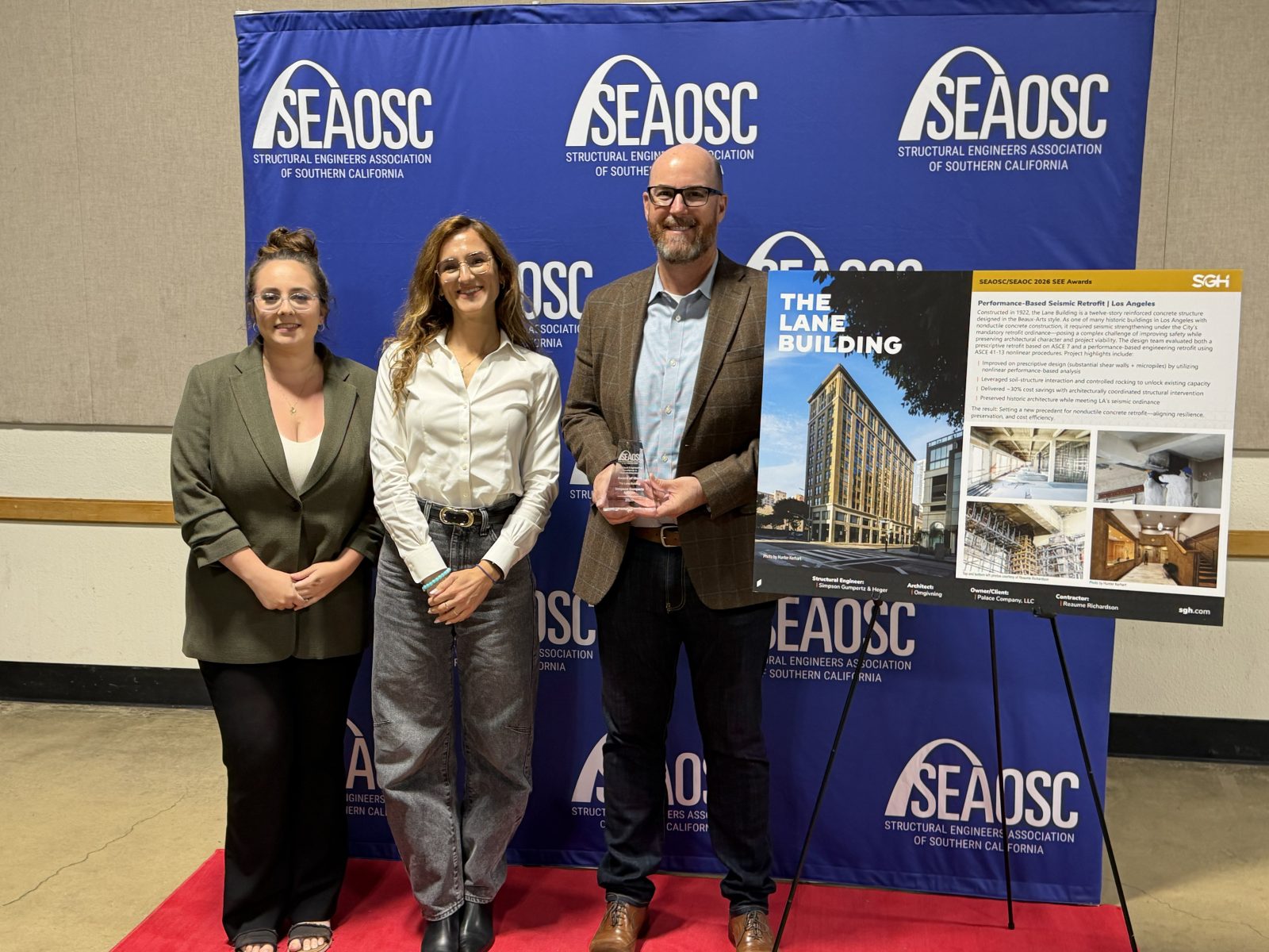 Three people pose with a trophy and an award board for The Lane Building at a SEAOSC event