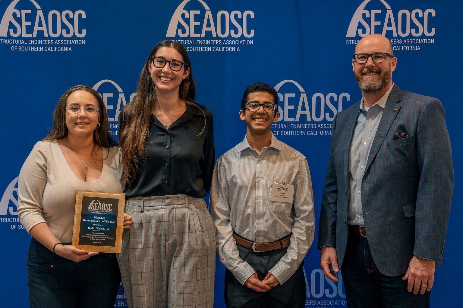 Four people pose at a SEAOSC event; a woman holds a Young Engineer of the Year award plaque