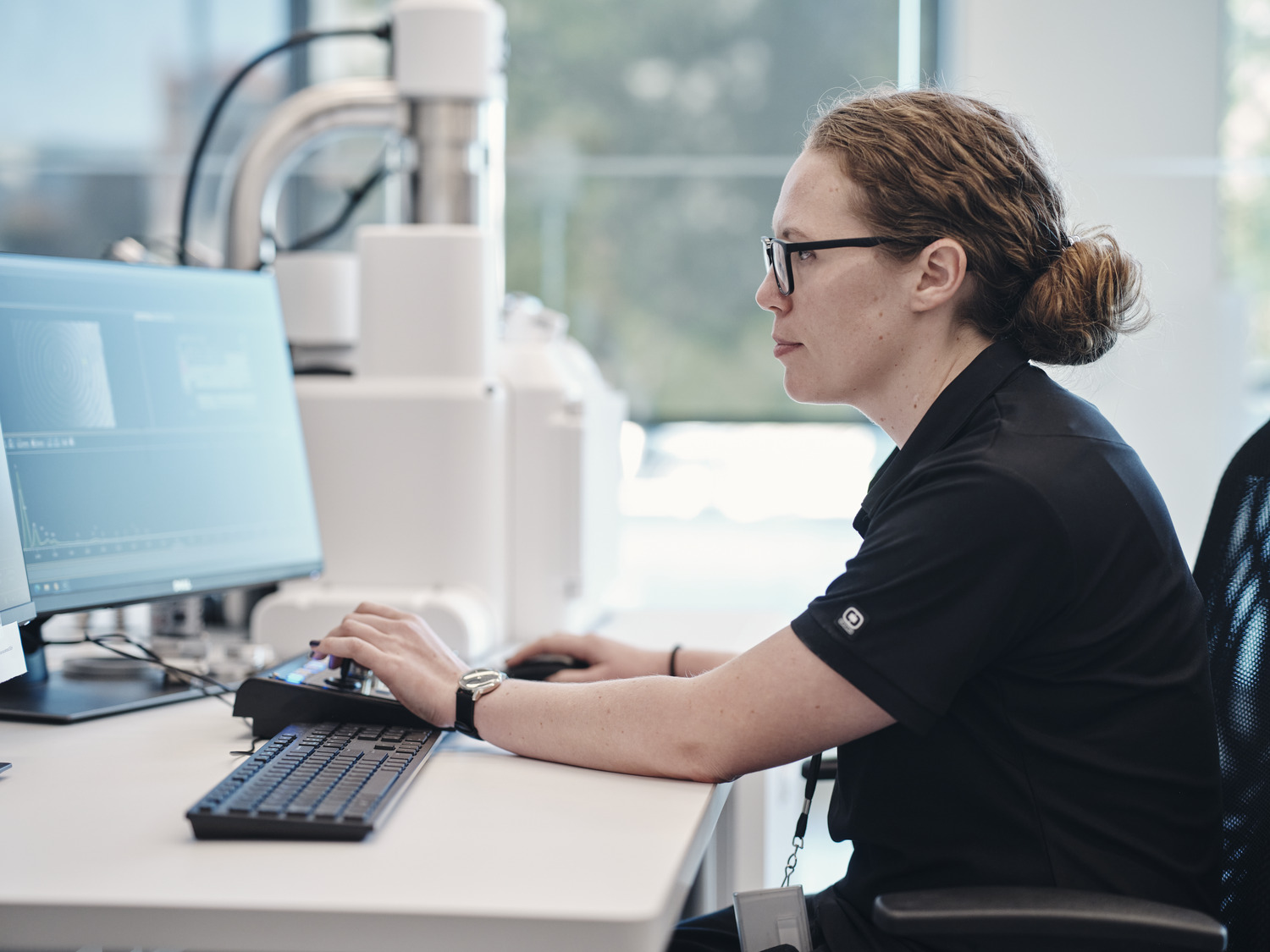 Researcher operating laboratory equipment while viewing data on a computer monitor